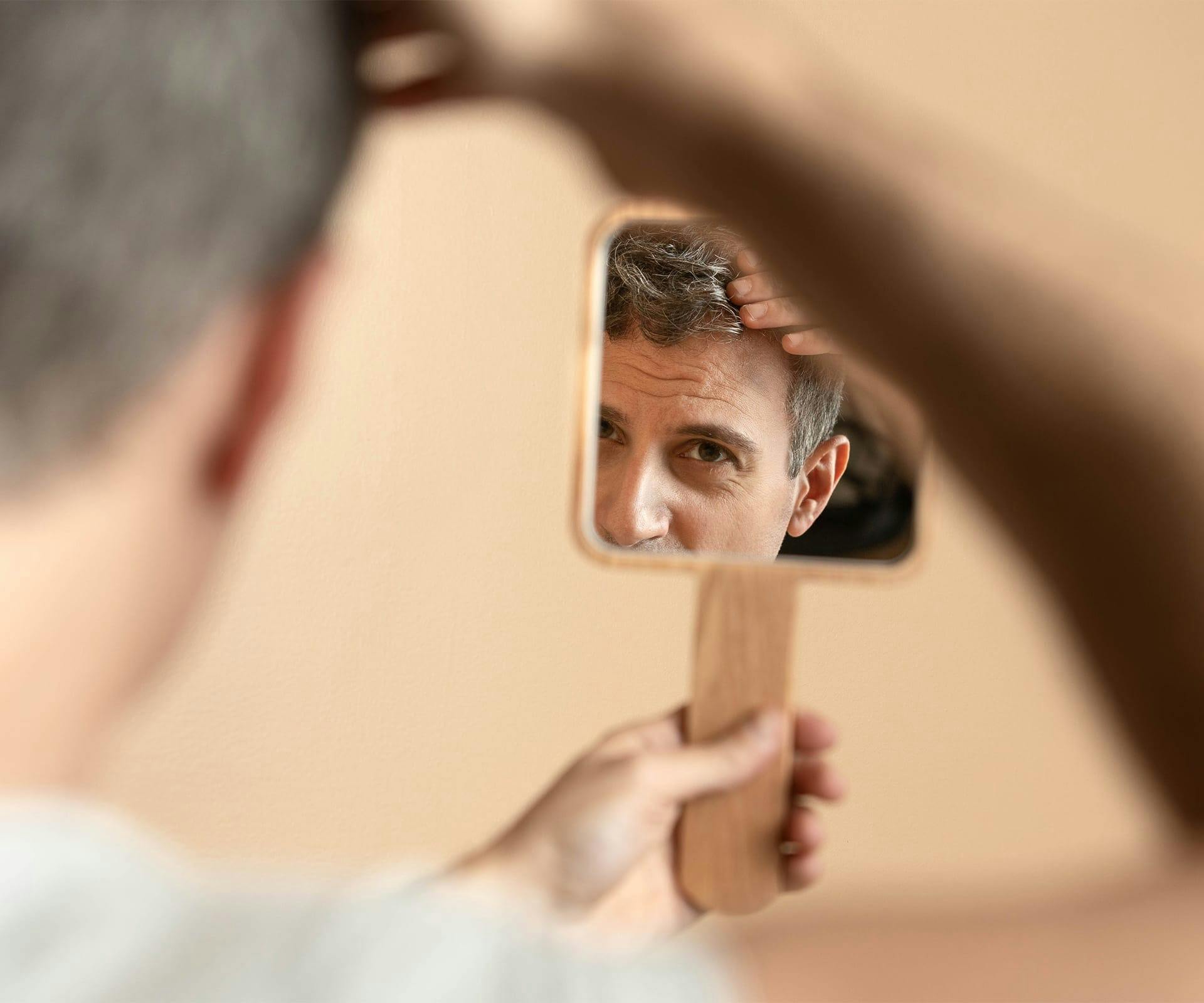 man looking through handheld mirror fixing his hair