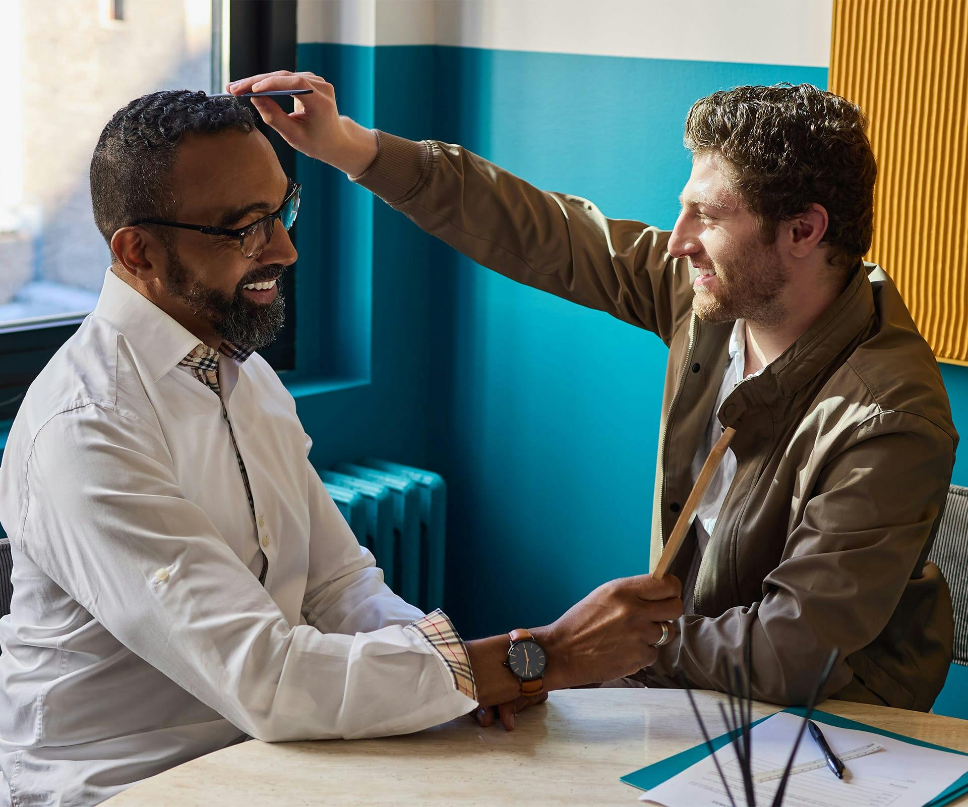 2 men facing eachother, laughing while one touches the others hair