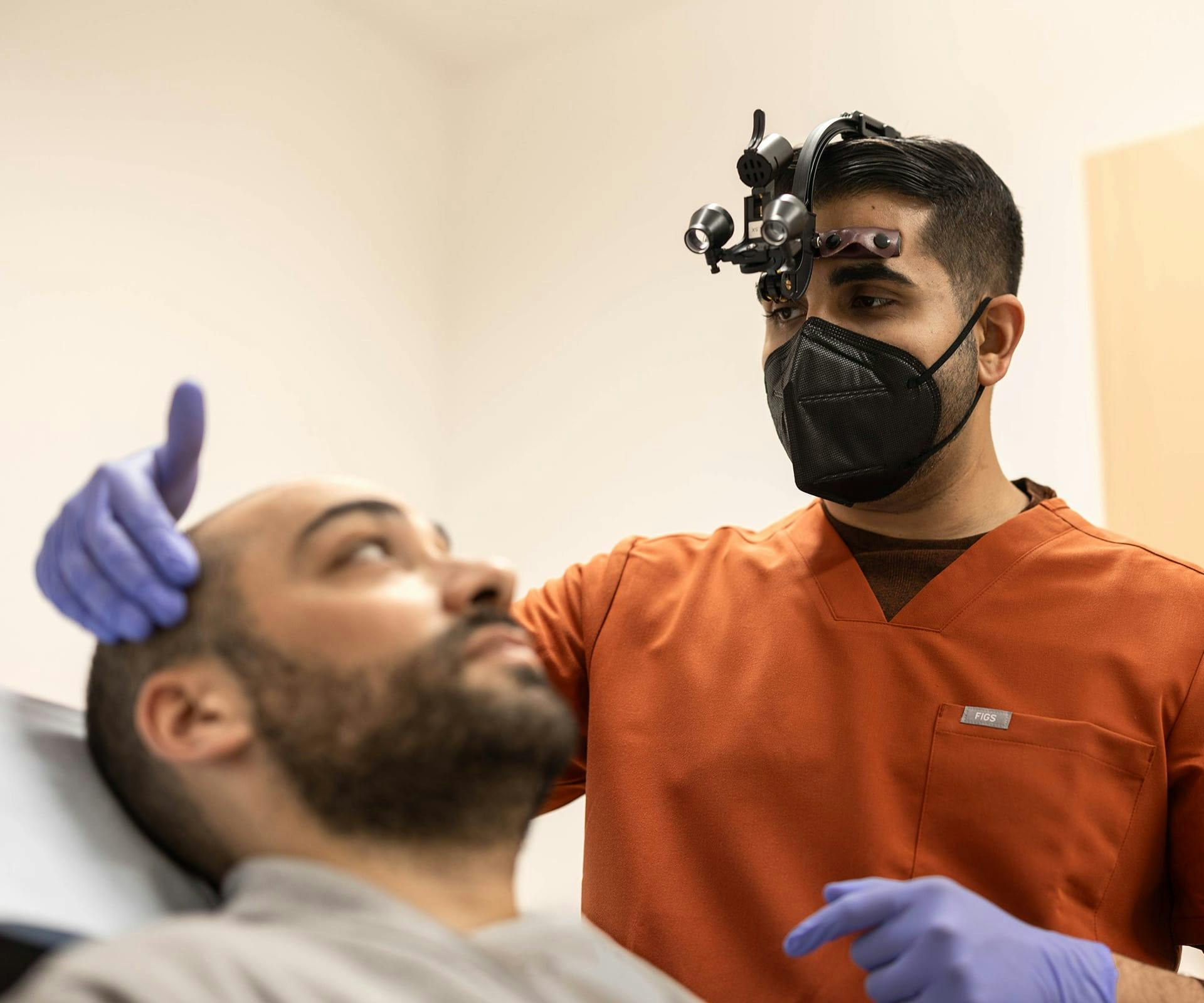 doctor with head gear looking at man's scalp while hes laying down