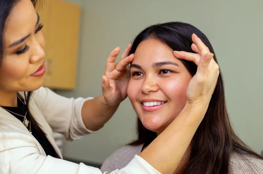 woman moving another woman's hair off her face to see her eyebrows
