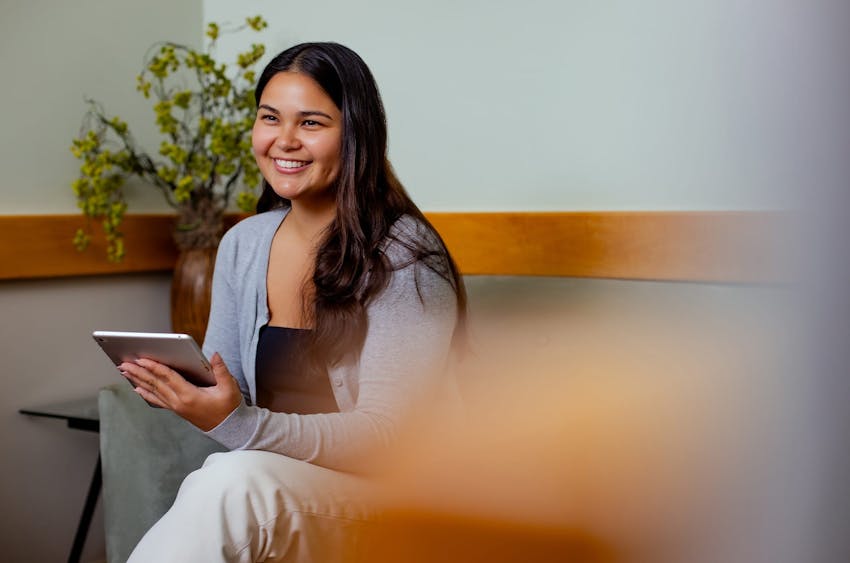 woman with ipad in hand smiling while sitting on couch
