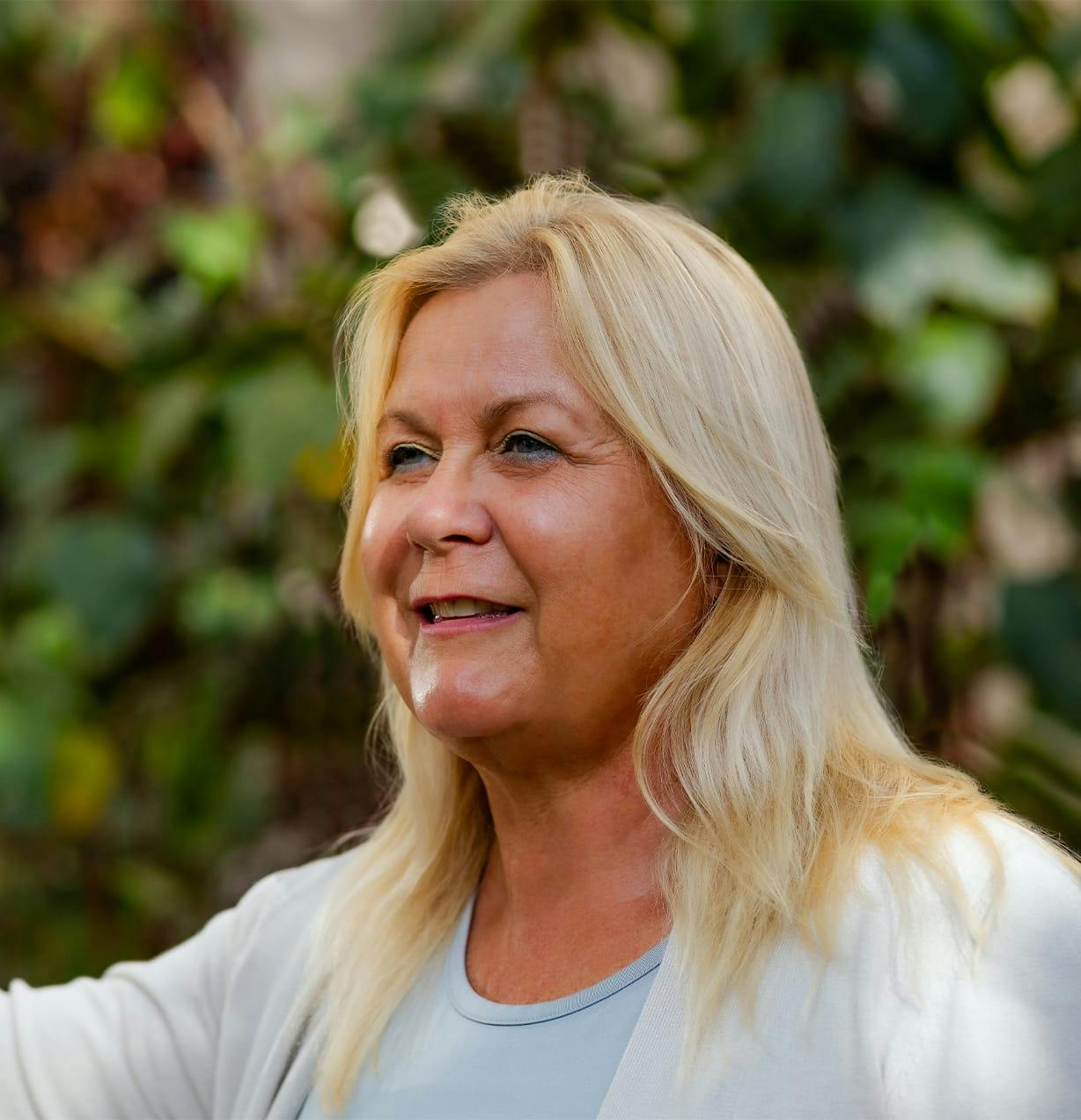 woman with blonde hair with greenery behind her