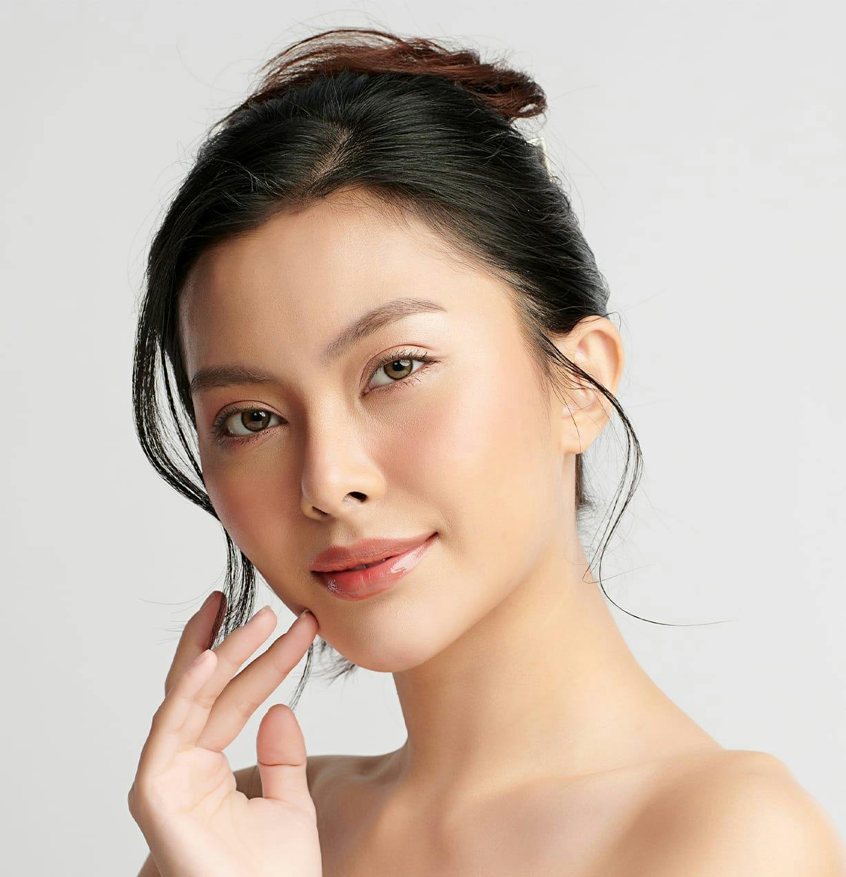 woman with her hair tied up with her finger on her cheek with a smile