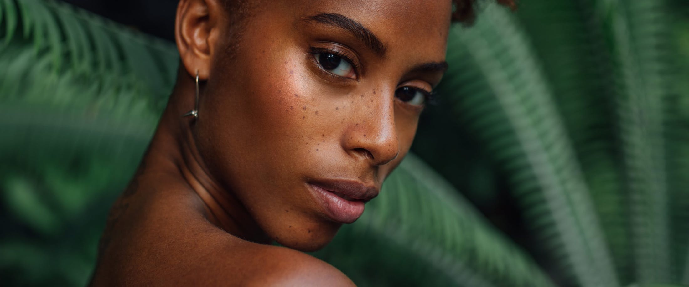 woman with freckles standing in front of a large green plant
