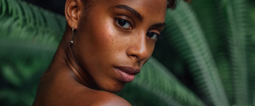 woman with freckles standing in front of a large green plant