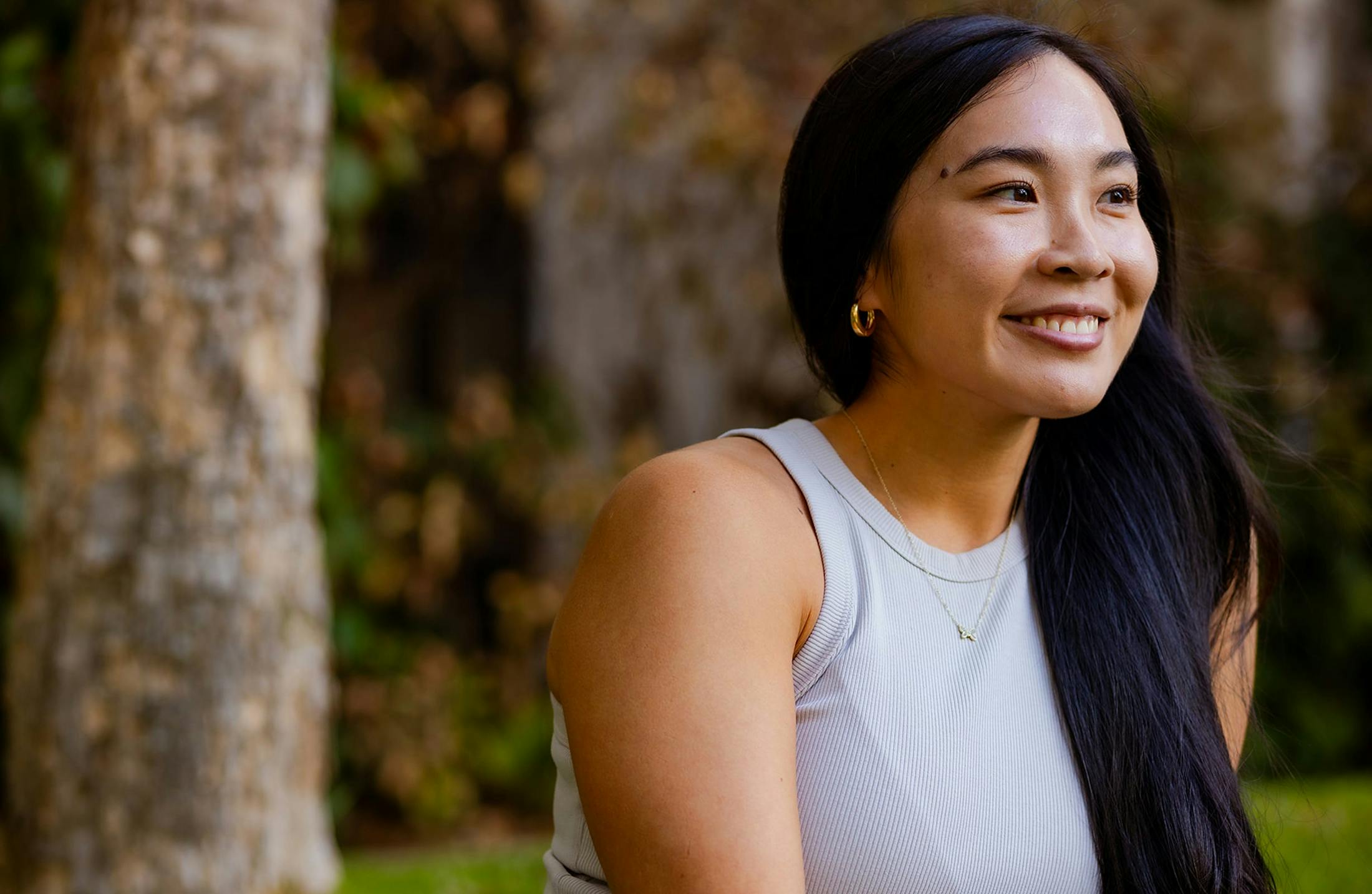 Black haired woman in white shirt with trees in the background.