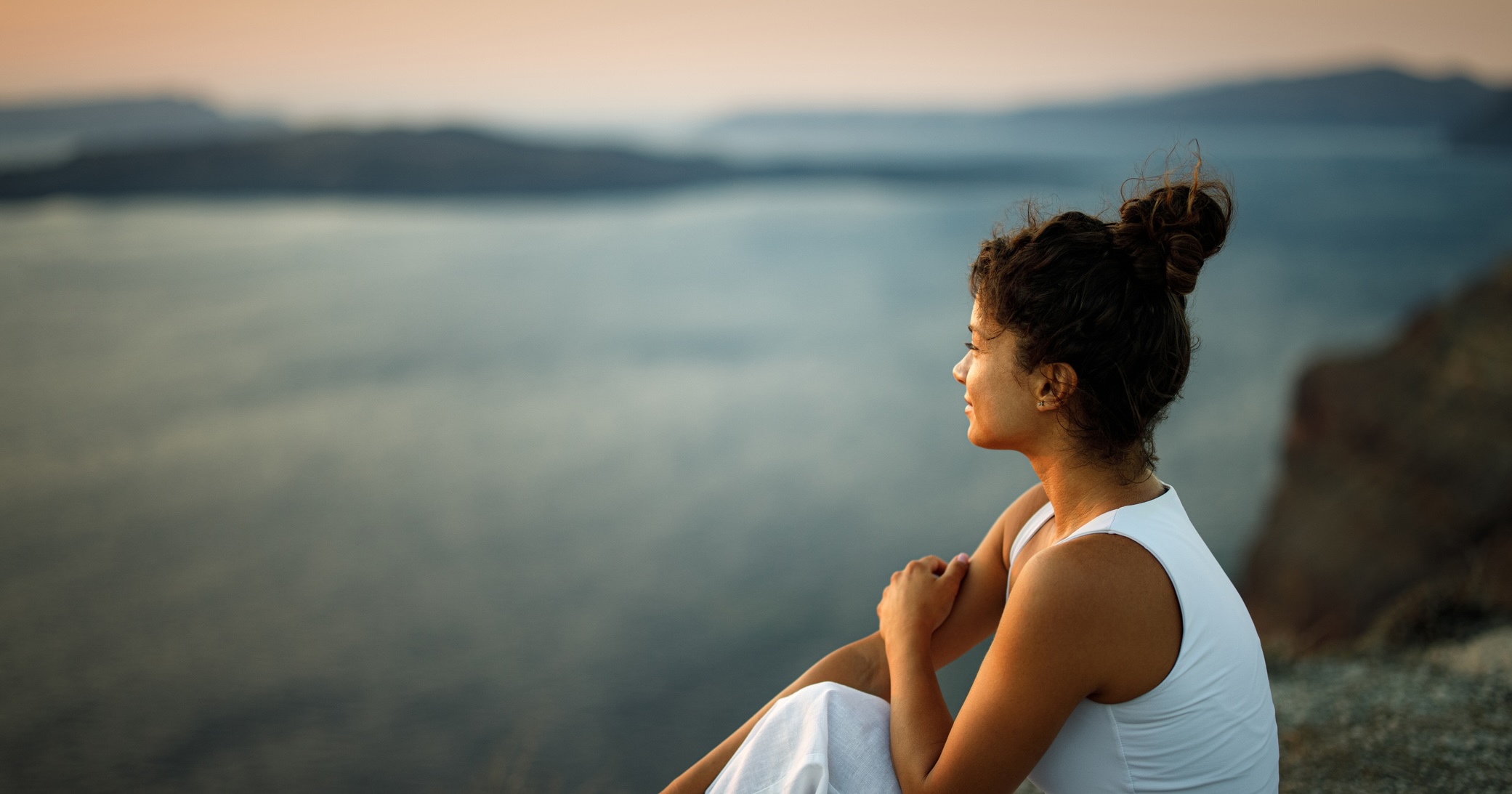 Woman sitting outdoors overlooking the water at sunset.
