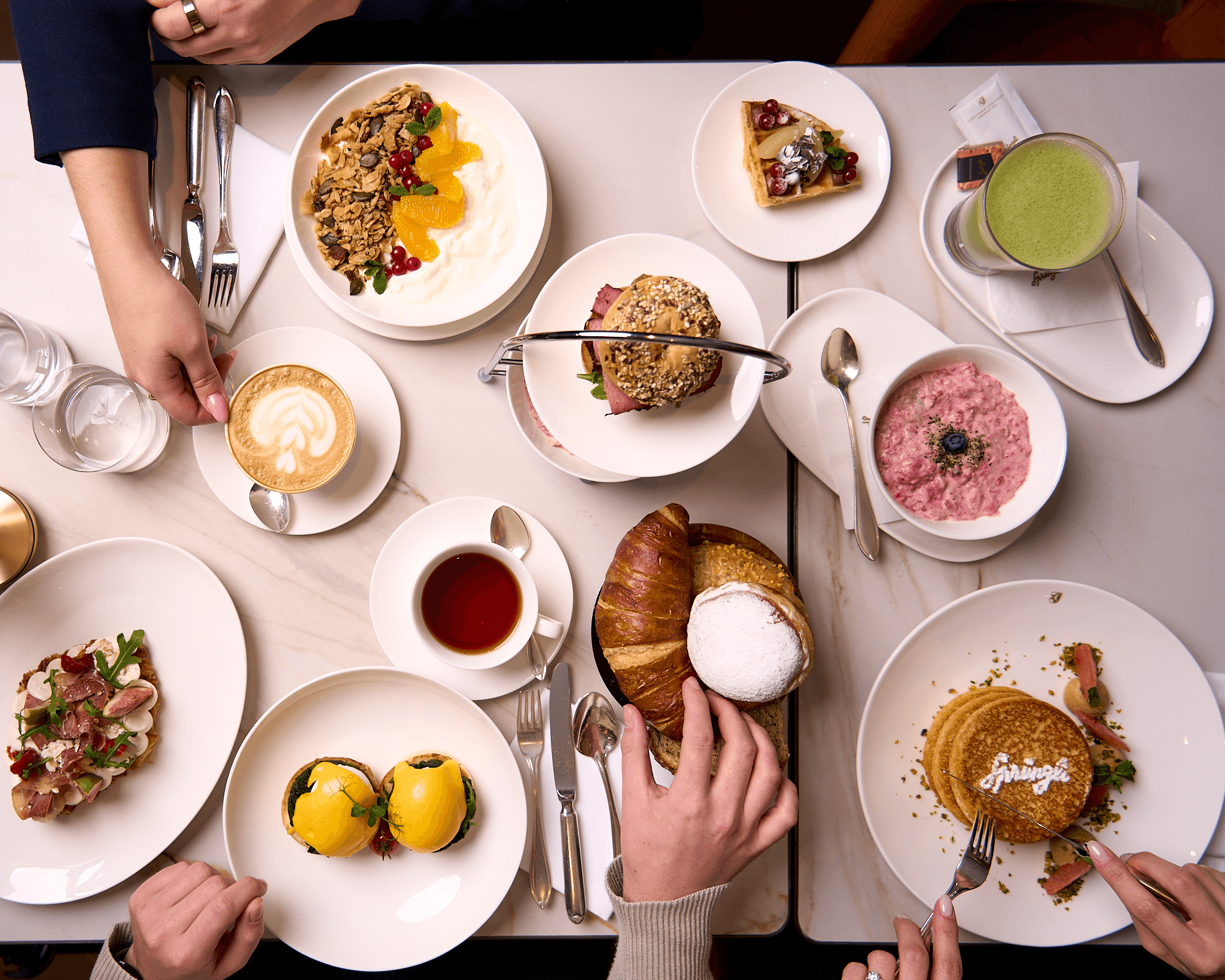 Confiserie Sprüngli Cafe und Restaurant Frühstückstisch mit diversen Speisen wie Pancakes, Eggs Benedict, Birchermüesli, Griechischer Joghurt mit Granola und Früchten sowie Getärnke wie Matcha, Kaffee und Tee
