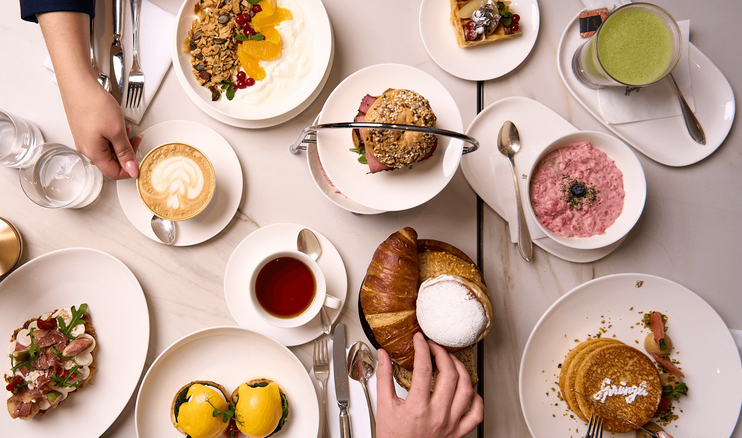 Confiserie Sprüngli Cafe und Restaurant Frühstückstisch mit diversen Speisen wie Pancakes, Eggs Benedict, Birchermüesli, Griechischer Joghurt mit Granola und Früchten sowie Getärnke wie Matcha, Kaffee und Tee