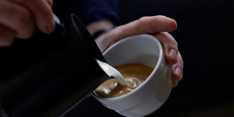 Hands pouring milk into coffee