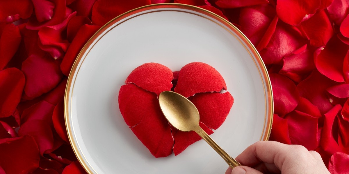Red cracked heart shaped food with spoon and red rose petals