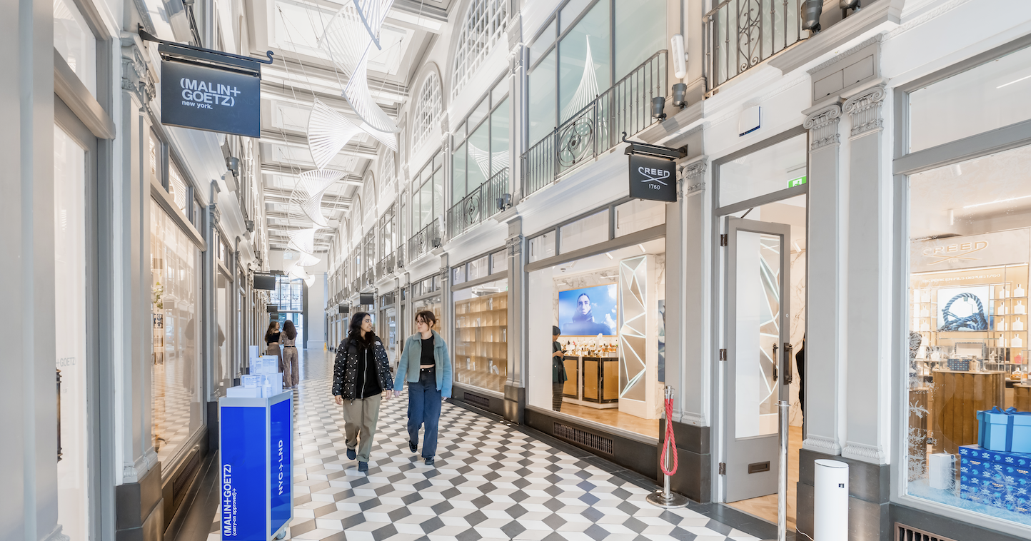 Two people walking through an arcade of shops