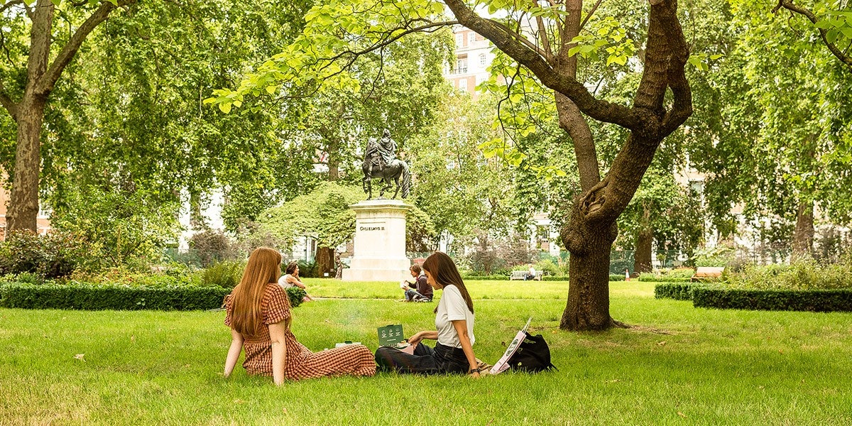 Two ladies sitting on the grass under trees