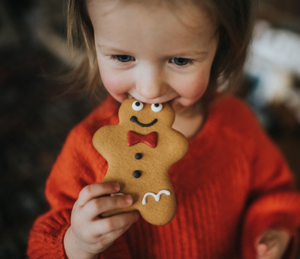 Girl in red jumper biting a gingerbread biscuit