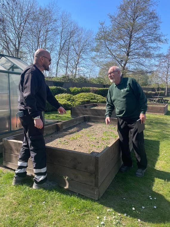 two people chatting next to a planter in a garden