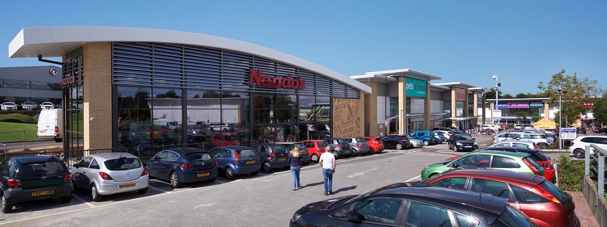 People walking in carpark with cards parked outside nandos