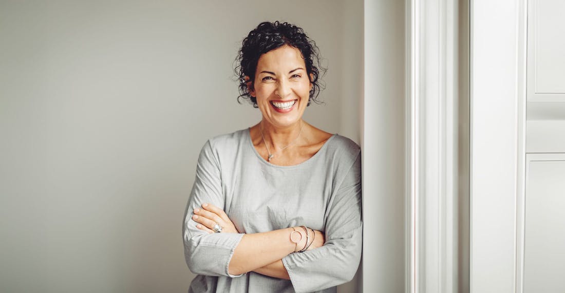 woman smiling while crossing her arms, wearing a grey shirt