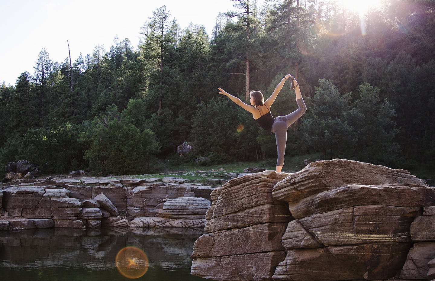 woman lifting her foot and pointing it upwards while standing on edge of river