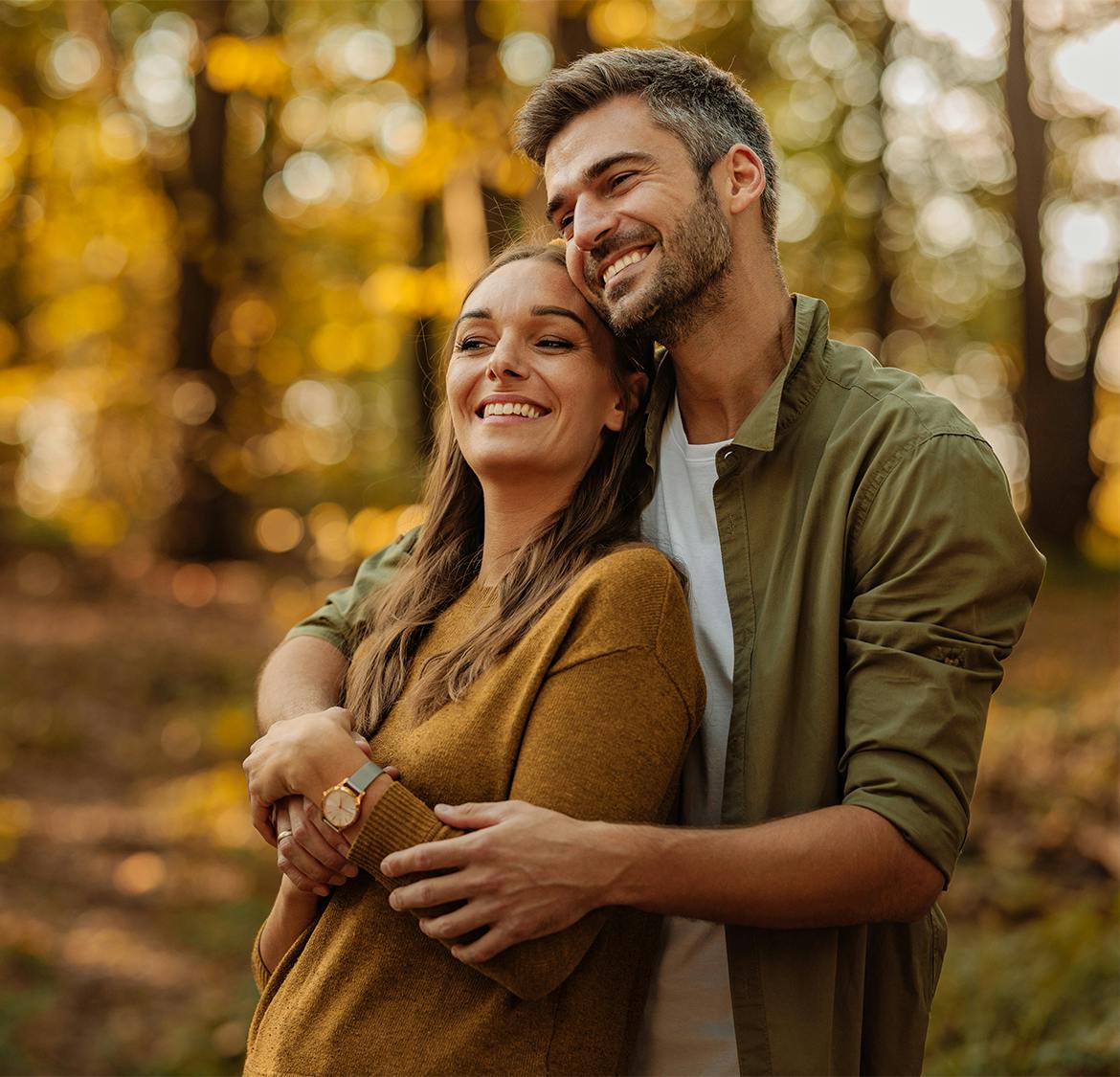 couple smiling and the man is hugging her from behind