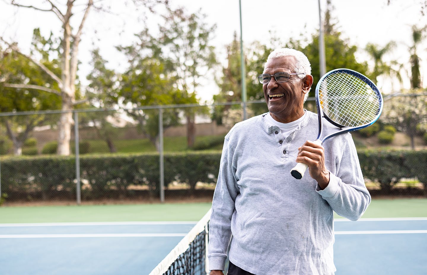 older man on tennis field holding a tennis rack