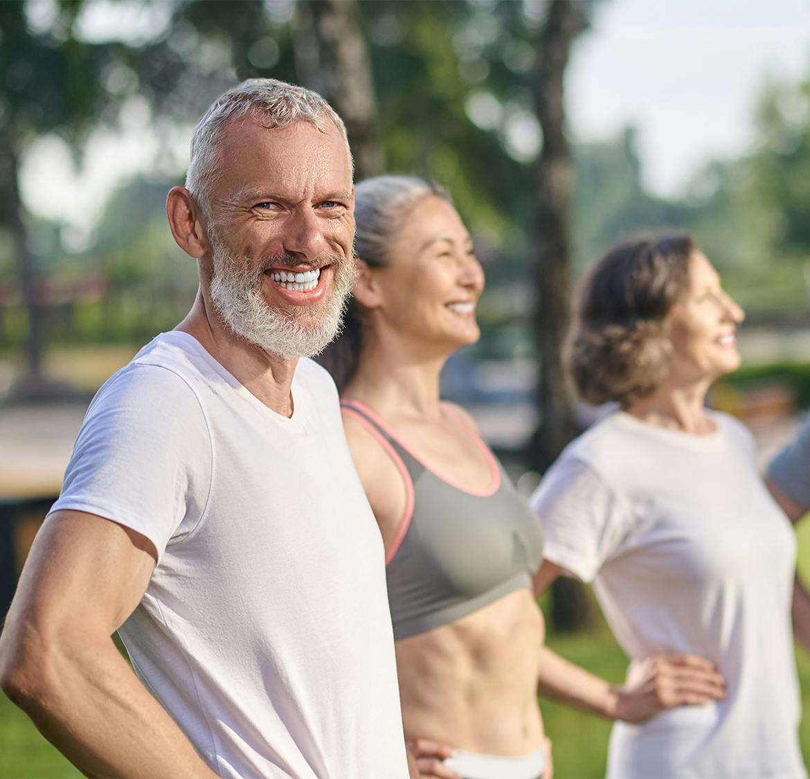 older man smiling with 2 women behind him as they all stretch