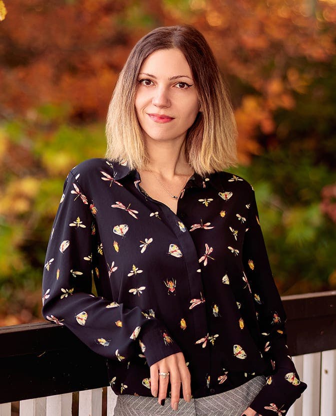Samantha Reichle in patterned top leaning on fence railing outside