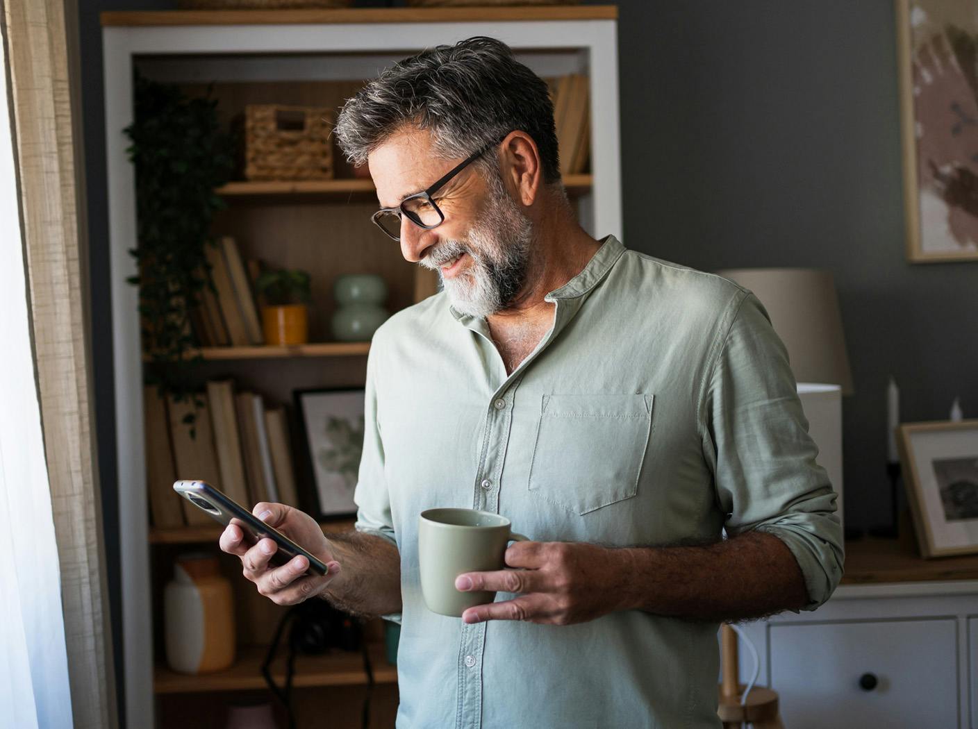 man holding a mug while looking at his phone