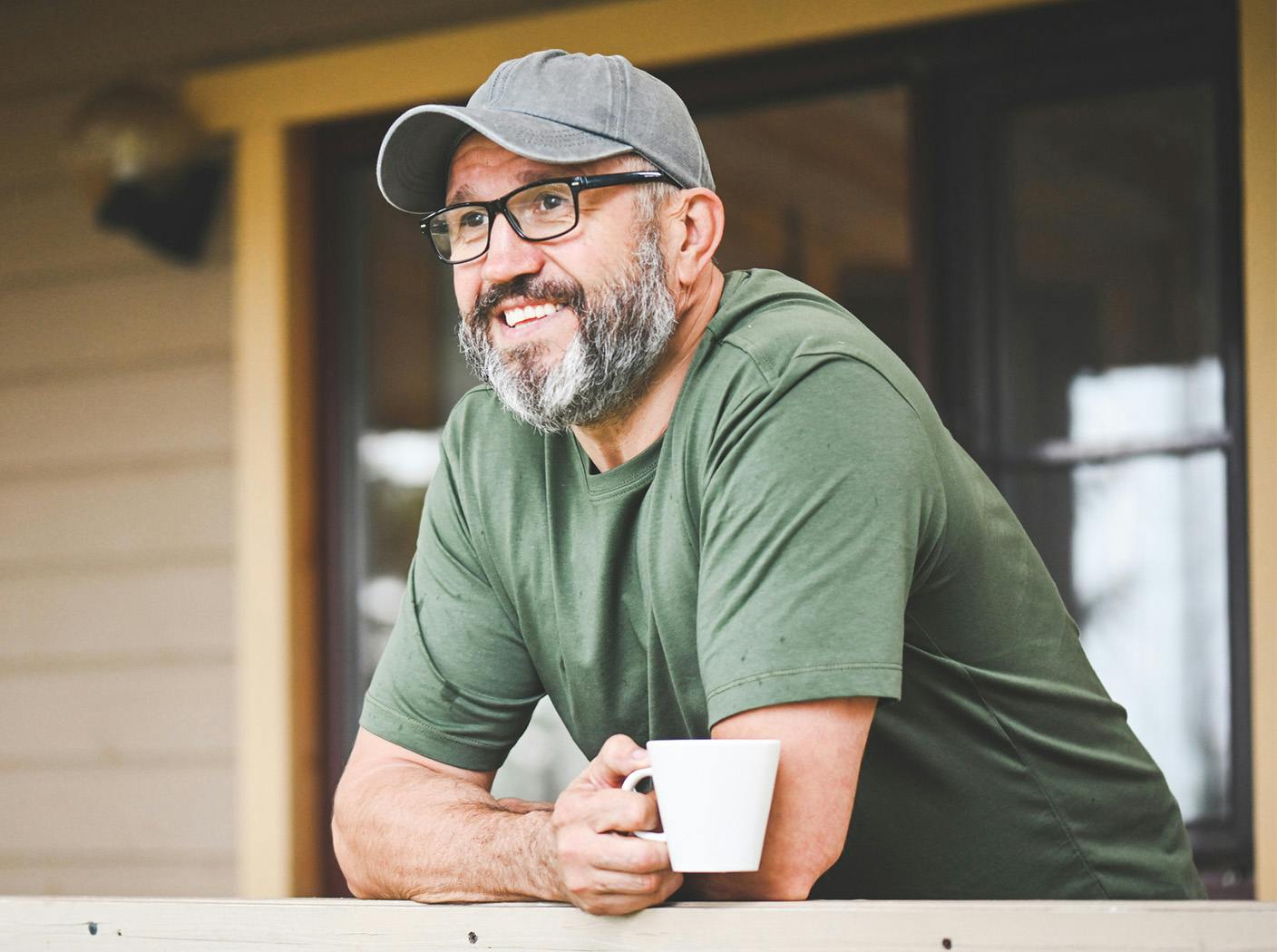 man leaning on fence railing with a cup of coffee