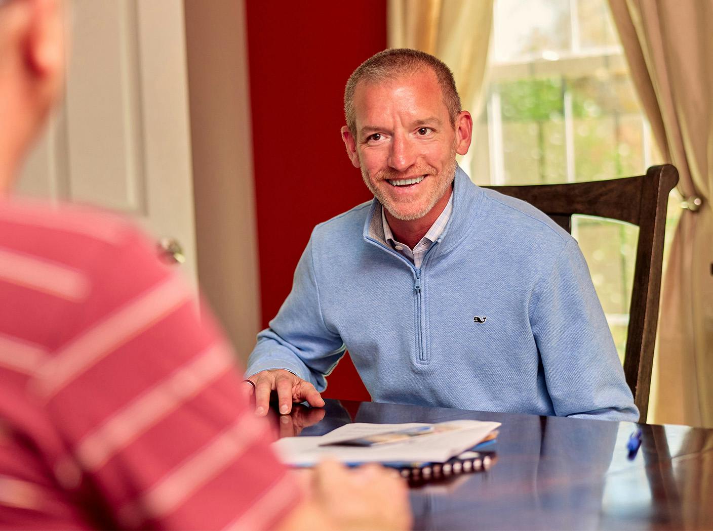 man sitting in chair smiling with paperwork in front of him