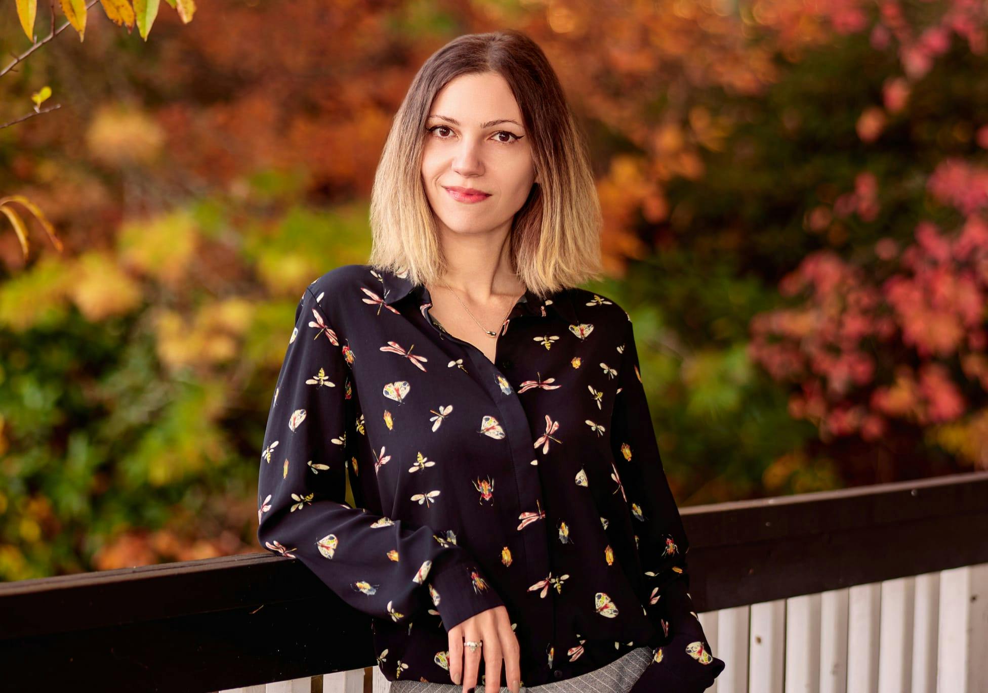Samantha Reichle in patterned top leaning on fence railing outside
