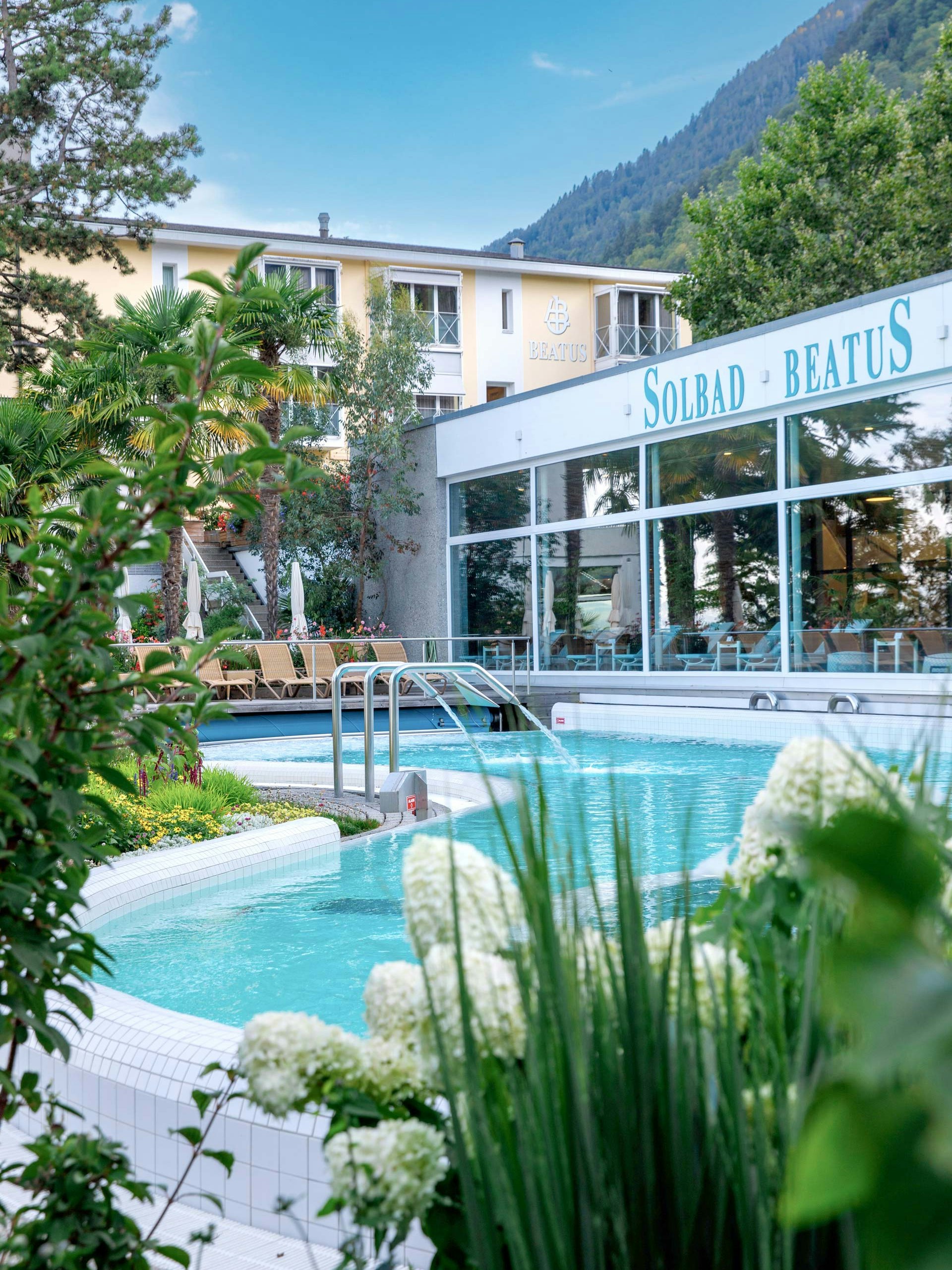 The Hotel BEATUS saltwater pool in summer Flowers and park landscape, on the left the Hotel Beatus, on the right the indoor swimming pool and the outdoor pool