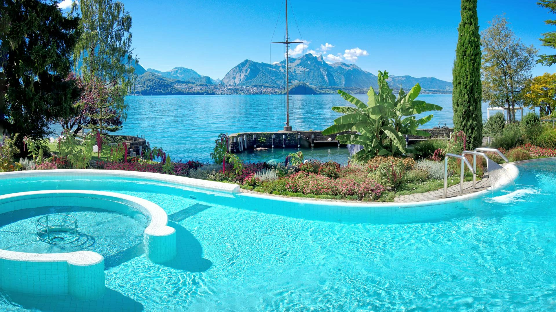 The Hotel BEATUS saltwater pool in summer Curved swimming pool, behind it Lake Thun and the mountains in summer