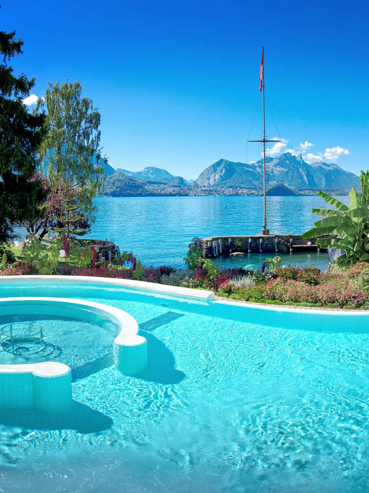 The Hotel BEATUS saltwater pool in summer Curved swimming pool, behind it Lake Thun and the mountains in summer