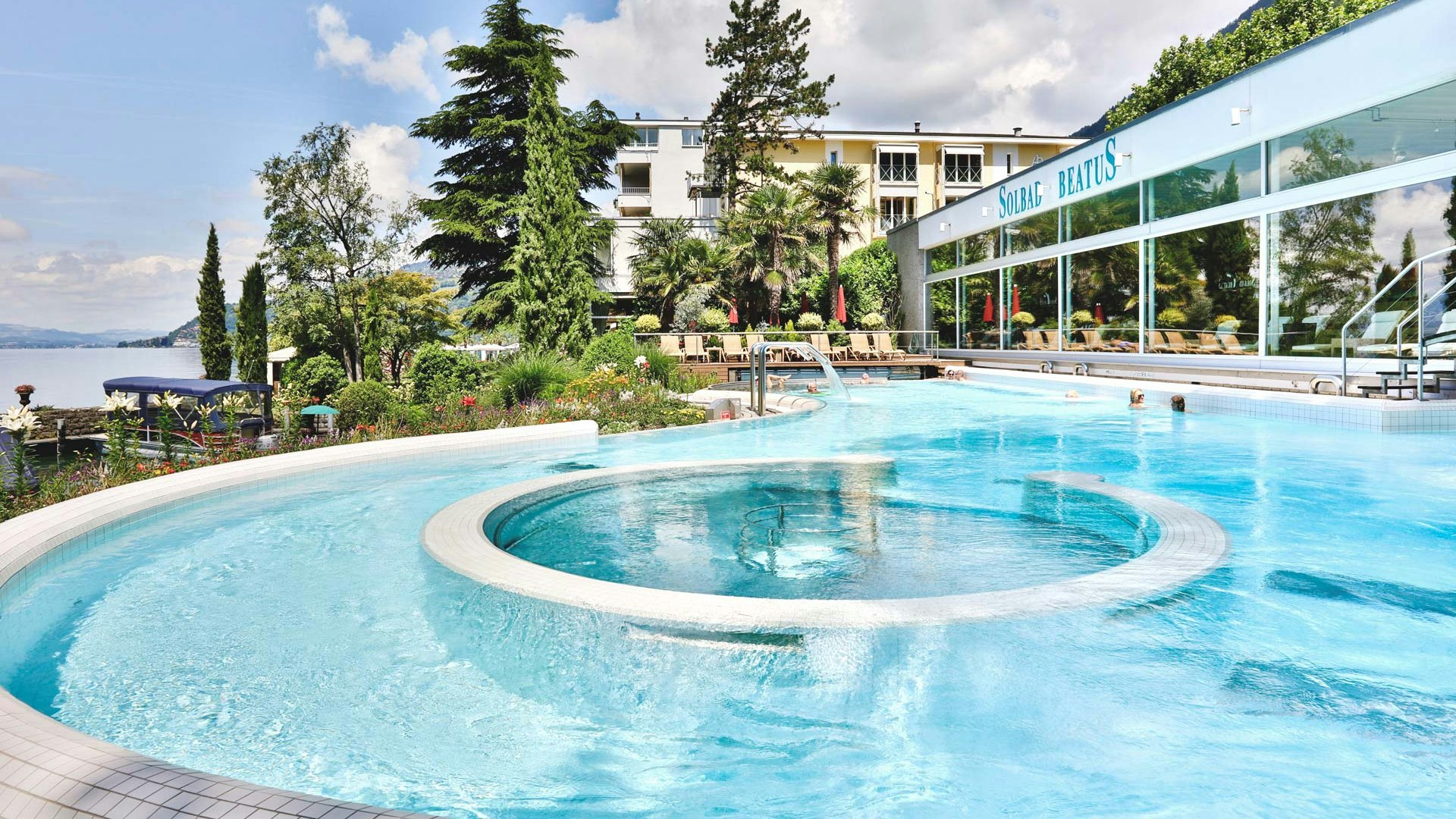 Solbad des Hotel BEATUS im Sommer Im Vordergrund ein Schwimmbad mit hellblauem Wasser, im Hintergrund Bäume und das Hotel Beatus