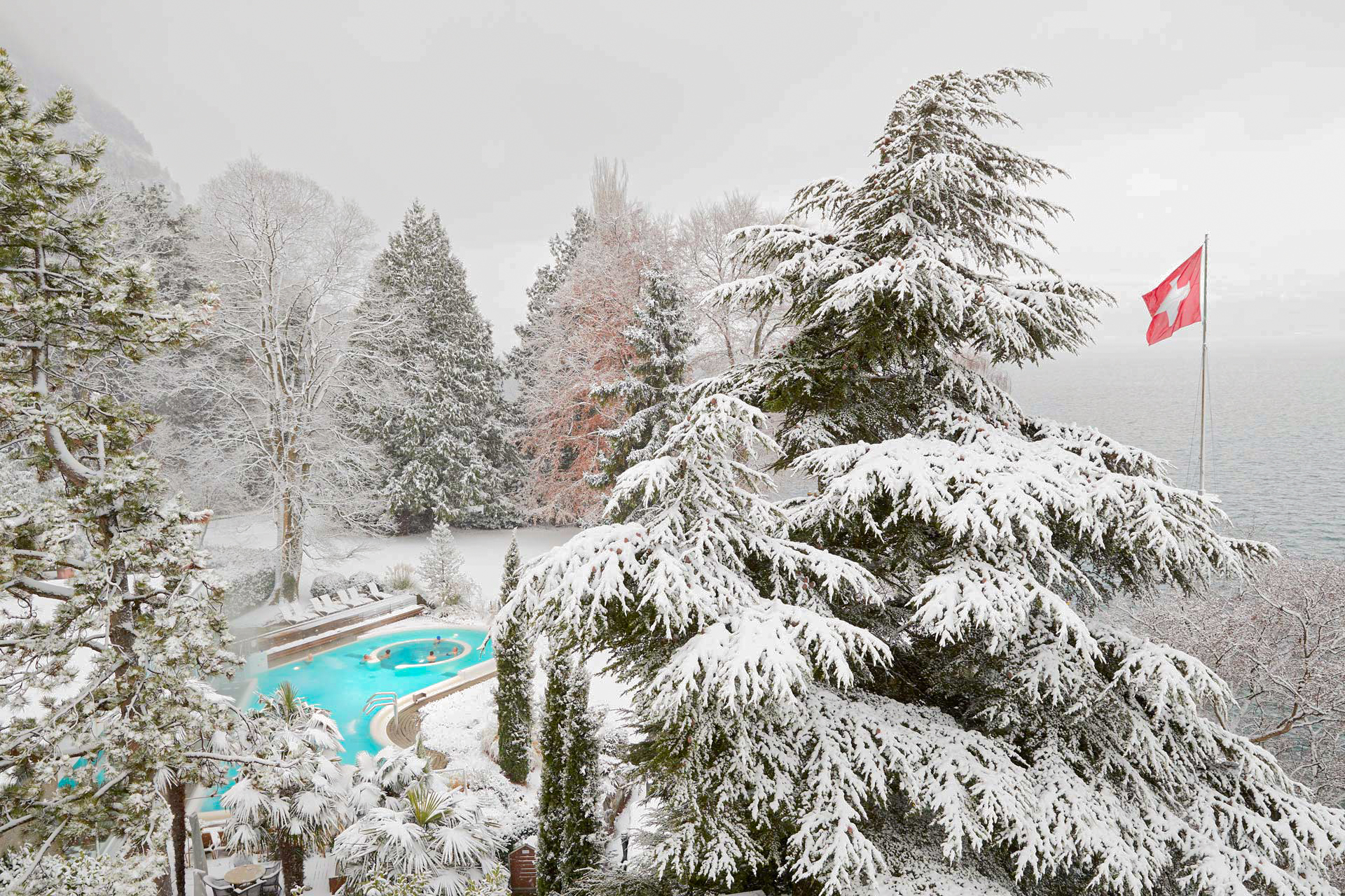 Verschneite Landschaft von schräg oben, links im Bild ein türkisfarbenes Schwimmbad