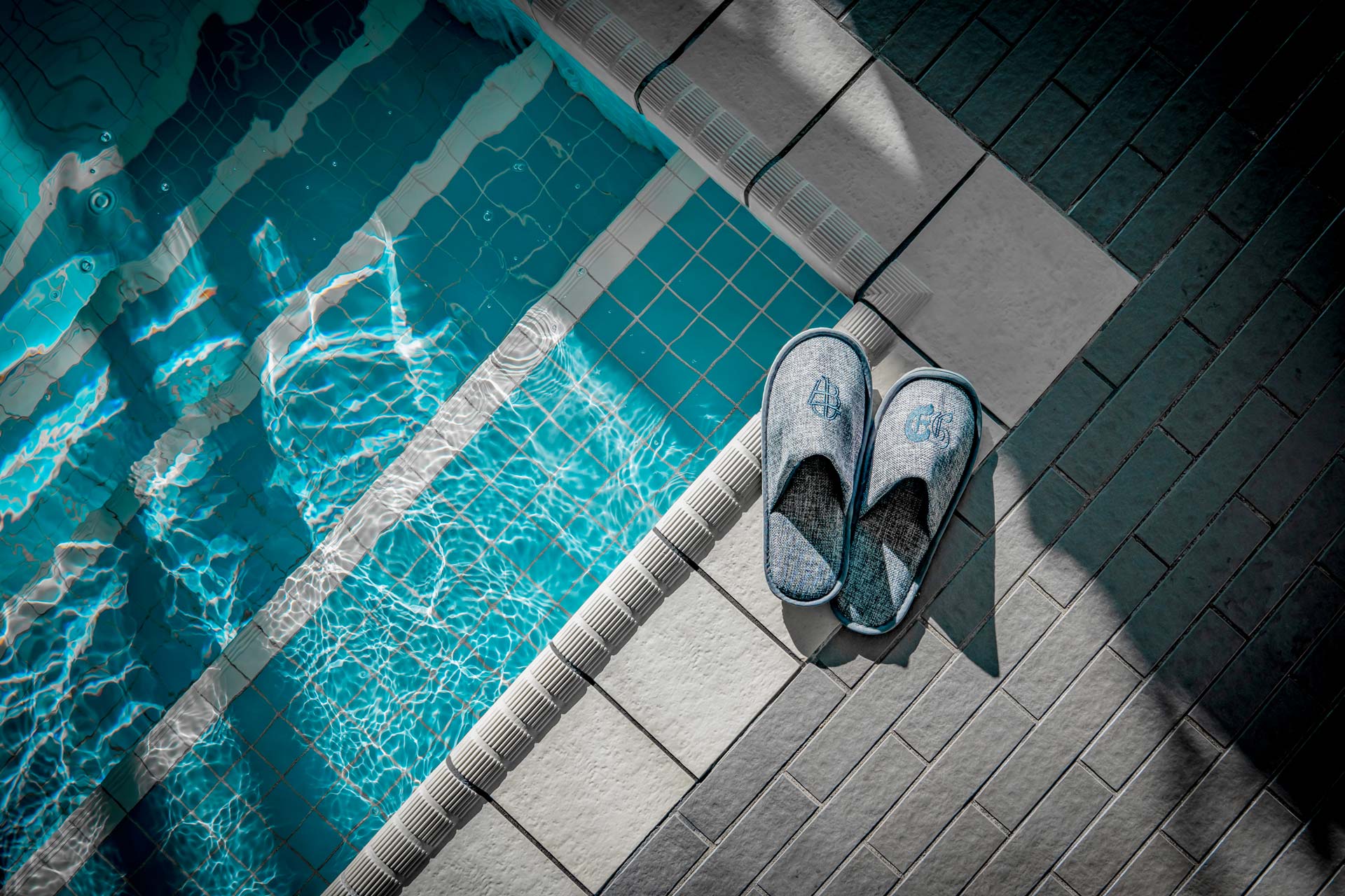 Details eines Schwimmbades von oben gesehen, davor am Rand Badeschlappen