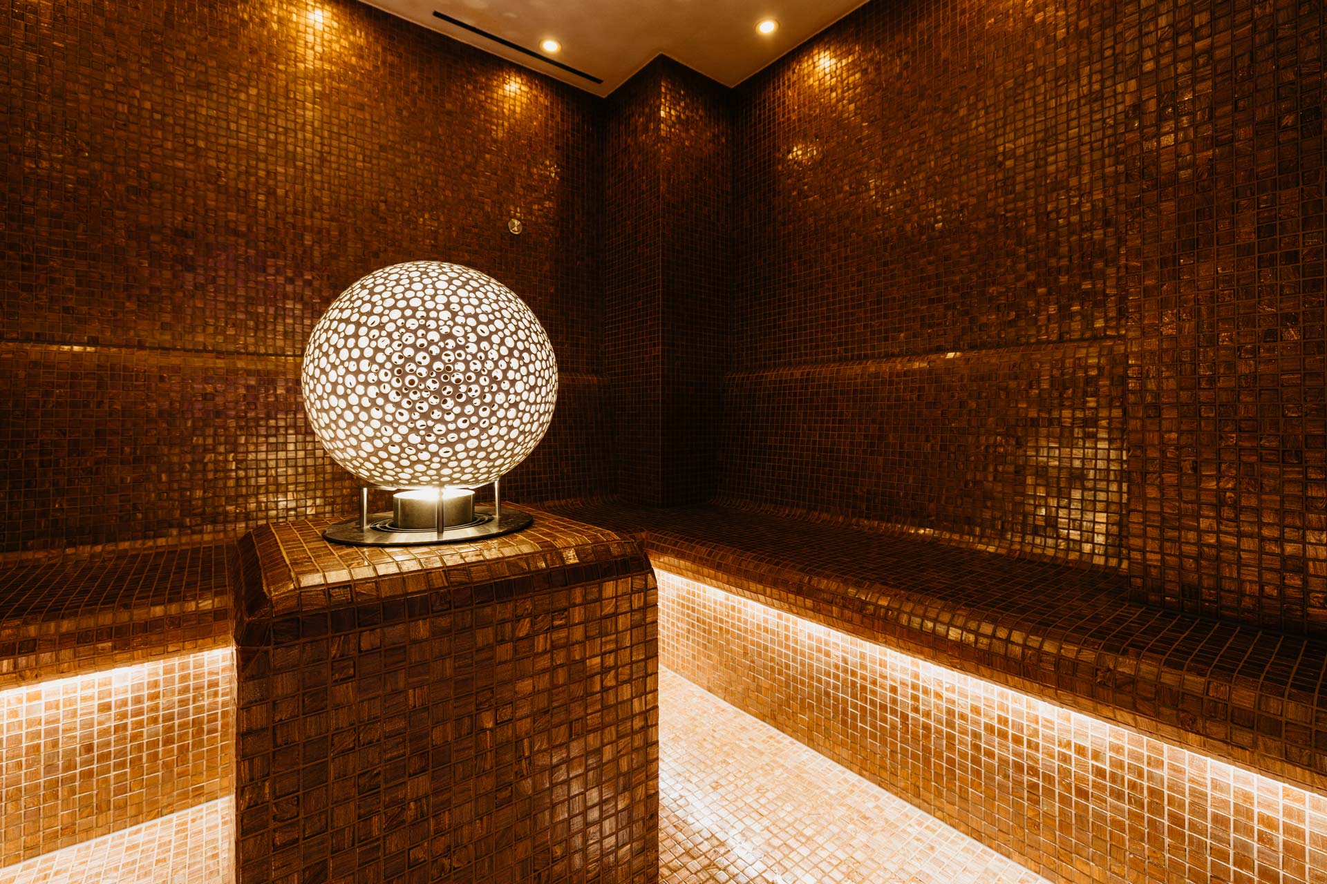Light sphere with small brown and white dots on a plinth, room covered with brown mosaic tiles
