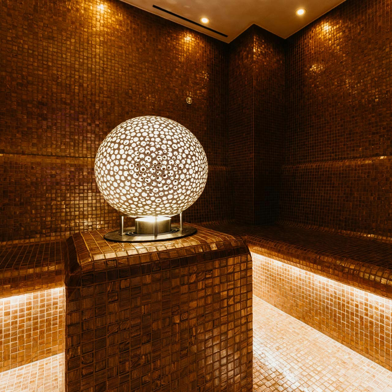 Lichtkugel im Aeris Dampfbad des Hotel BEATUS Lichtkugel mit kleinen braun-weissen Punkten auf Sockel, Raum mit braunen Mosaikfliesen ausgelegt