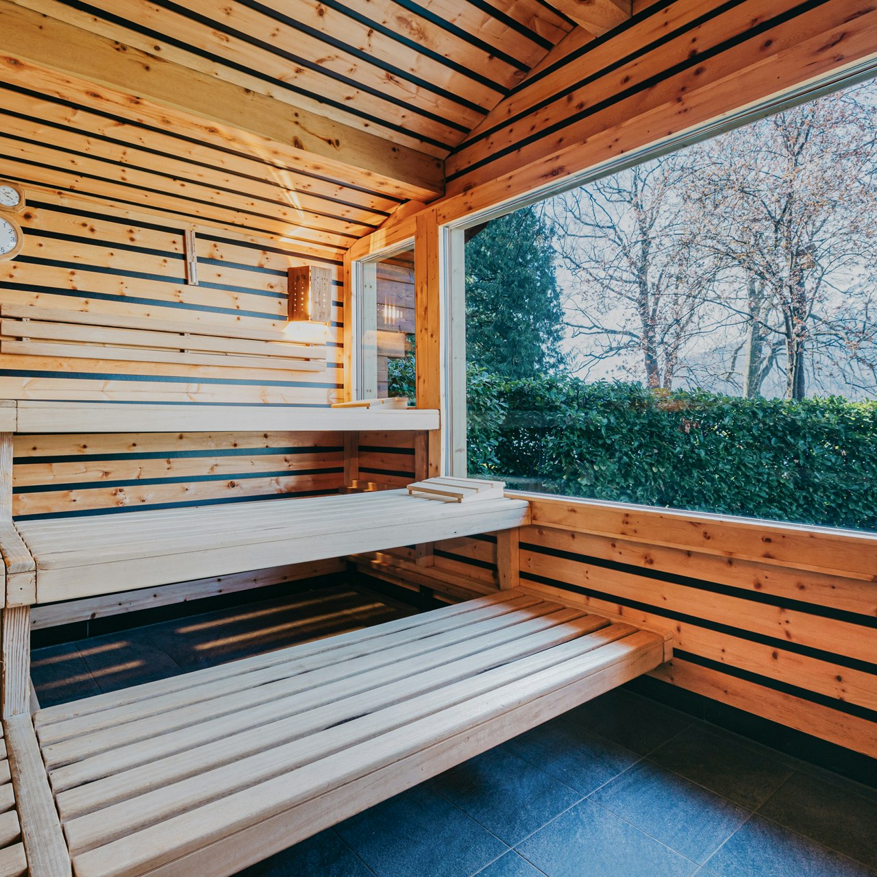 Sauna extérieur Finnicum avec vue sur le lac Cabine de sauna entièrement revêtue de bois et sol en pierre, grande fenêtre donnant sur le lac