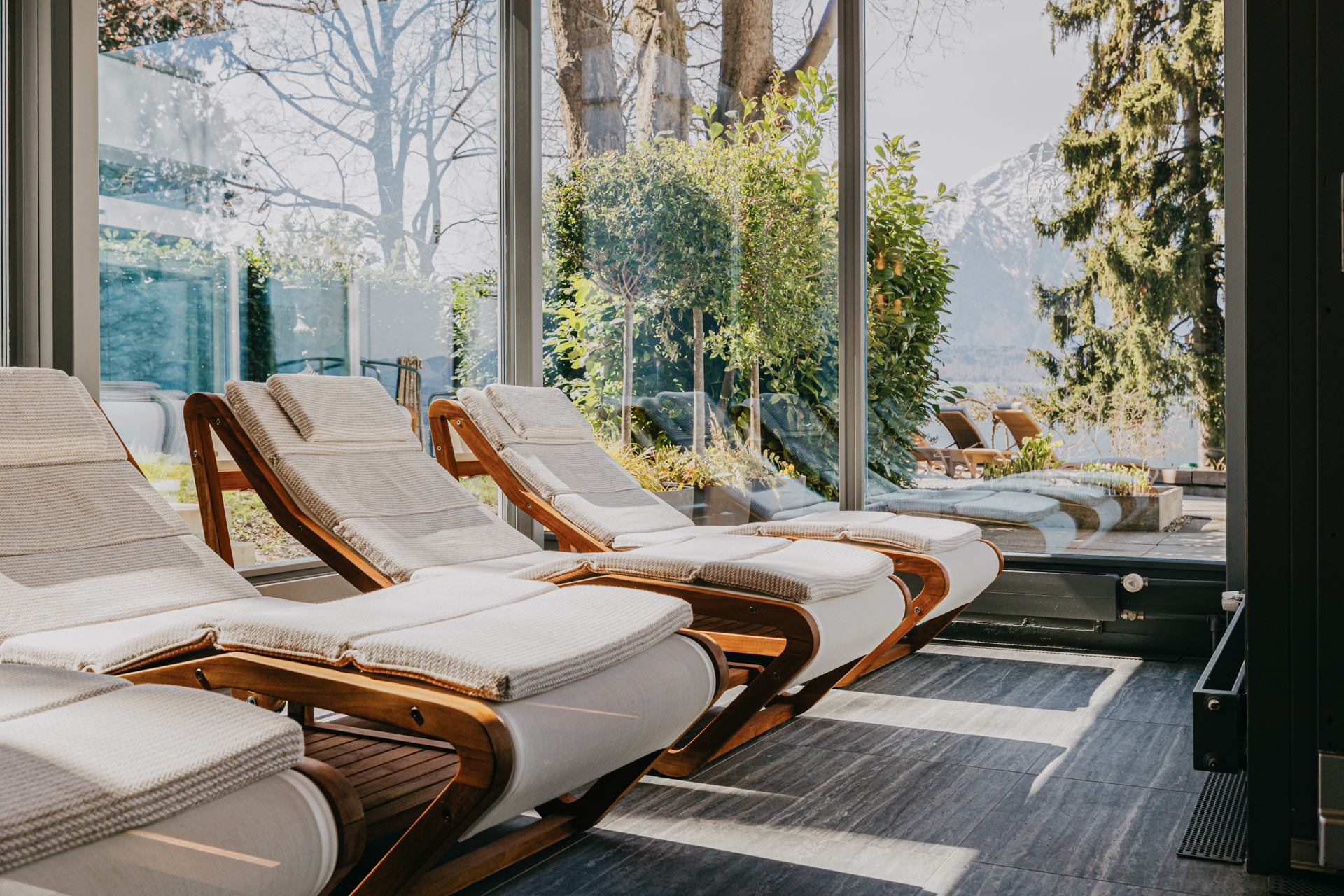 Weich gepolsterte Liegen, dahinter ein grosses Fenster mit Blick auf den Hotelpark und See