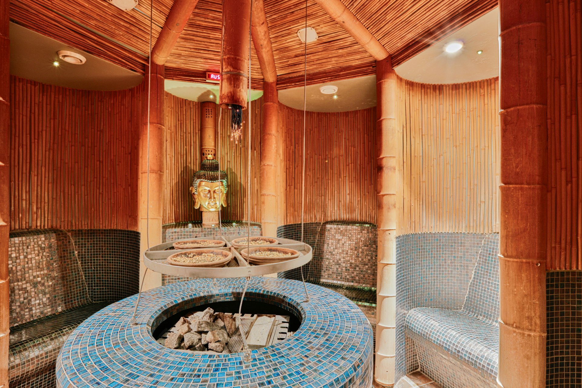 Sauna with infusion stove in the centre, left and right seating cabins lined with mosaics in brown and blue respectively, a Buddha figure at the back