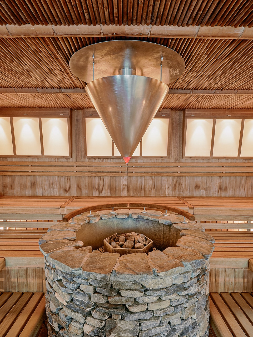 Zen-Sauna im Hotel BEATUS Grosser Metallkegel für automatischen Aufguss über rundem Saunaofen aus Stein, rundherum Sitzbänke, kleine Panoramafenster