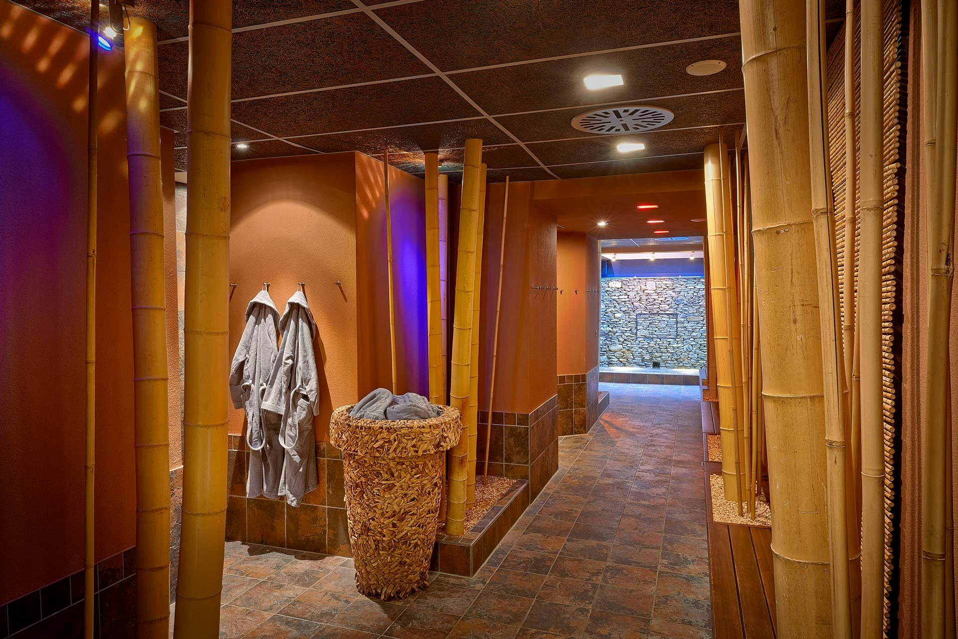 Corridor with bamboo poles, two bathrobes hanging on the left, a wall of stones at the very back