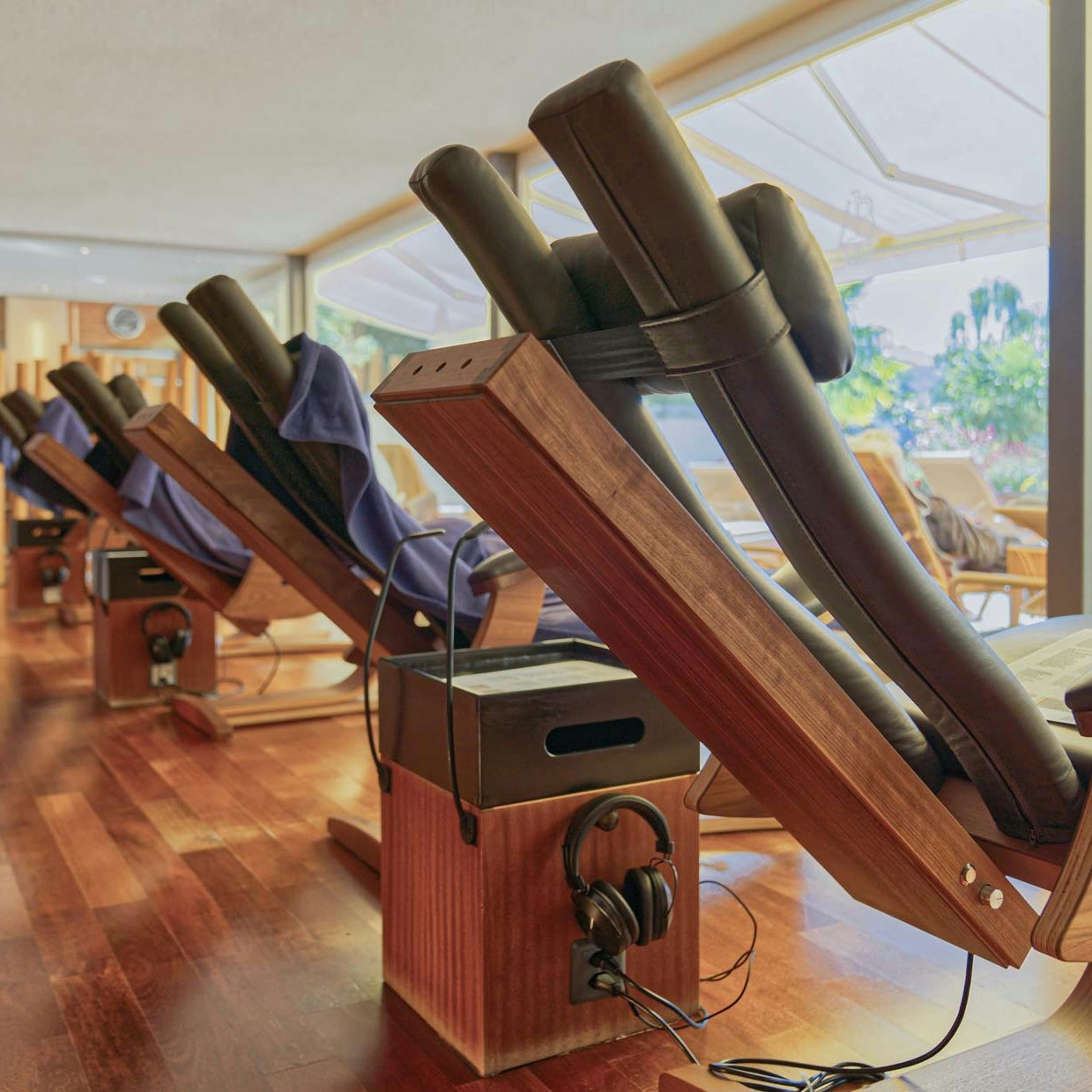 Chaises infrarouges et installation musicale dans le sauna de l'hôtel BEATUS Chaises longues en cuir et en bois avec vue sur l'extérieur, à côté d'un haut-parleur avec écouteurs,