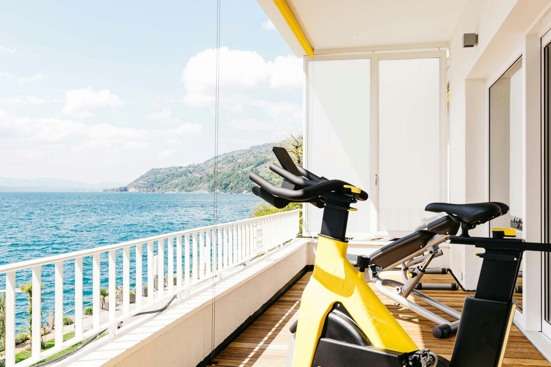 Gelbes Fitnessfahrrad und Trainingsbank auf Balkon mit Blick auf den Thunersee