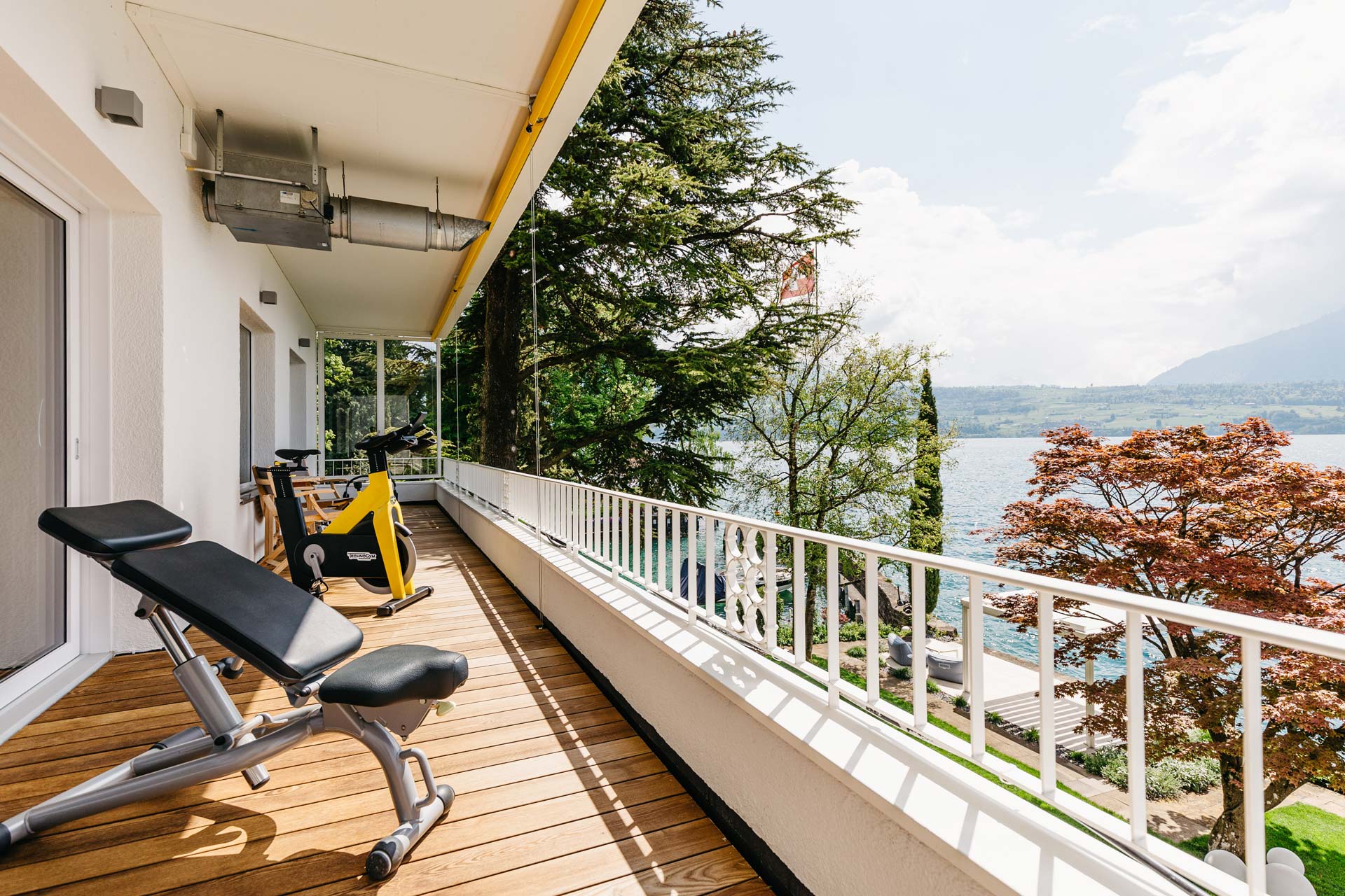 Banc d'entraînement et vélo de fitness jaune sur le balcon avec vue sur le lac de Thoune