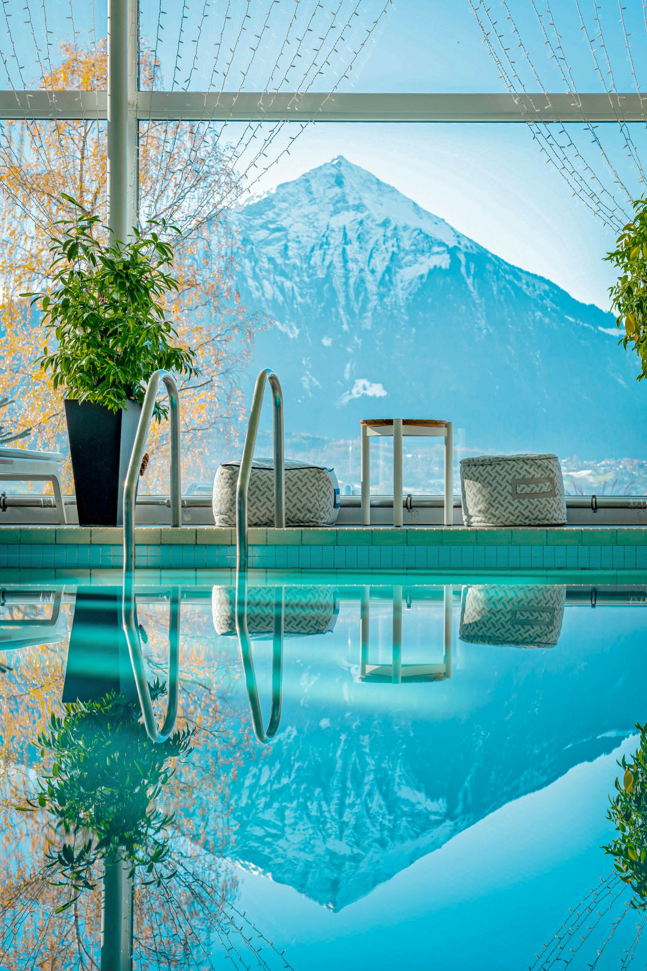 Vorne sieht man nur Wasser vom Hallenbad, darin spiegelt sich der Berg, den man hinter dem Fenster sieht