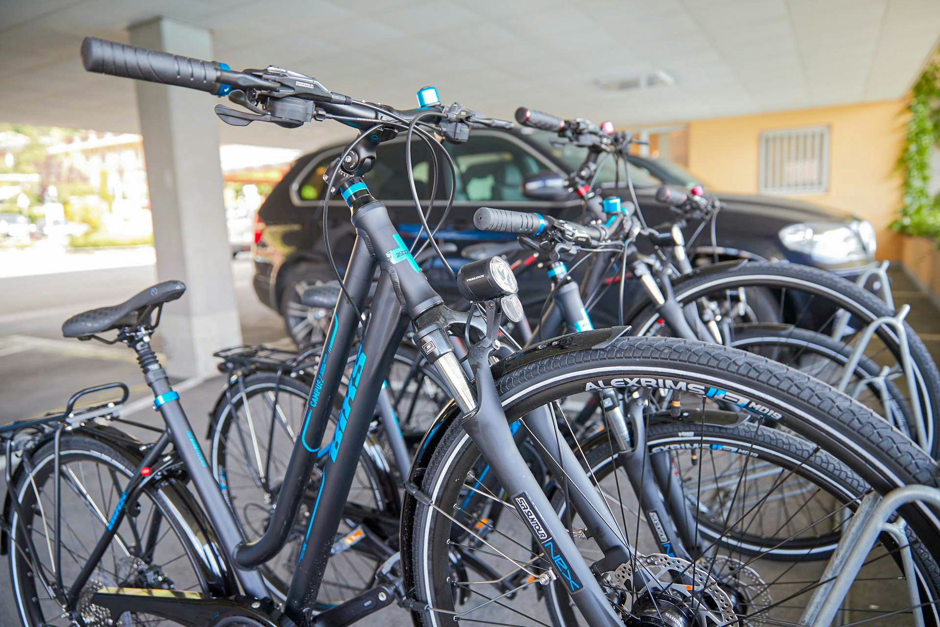Vier Fahrräder in Fahrradständern, dahinter ein geparkte Auto