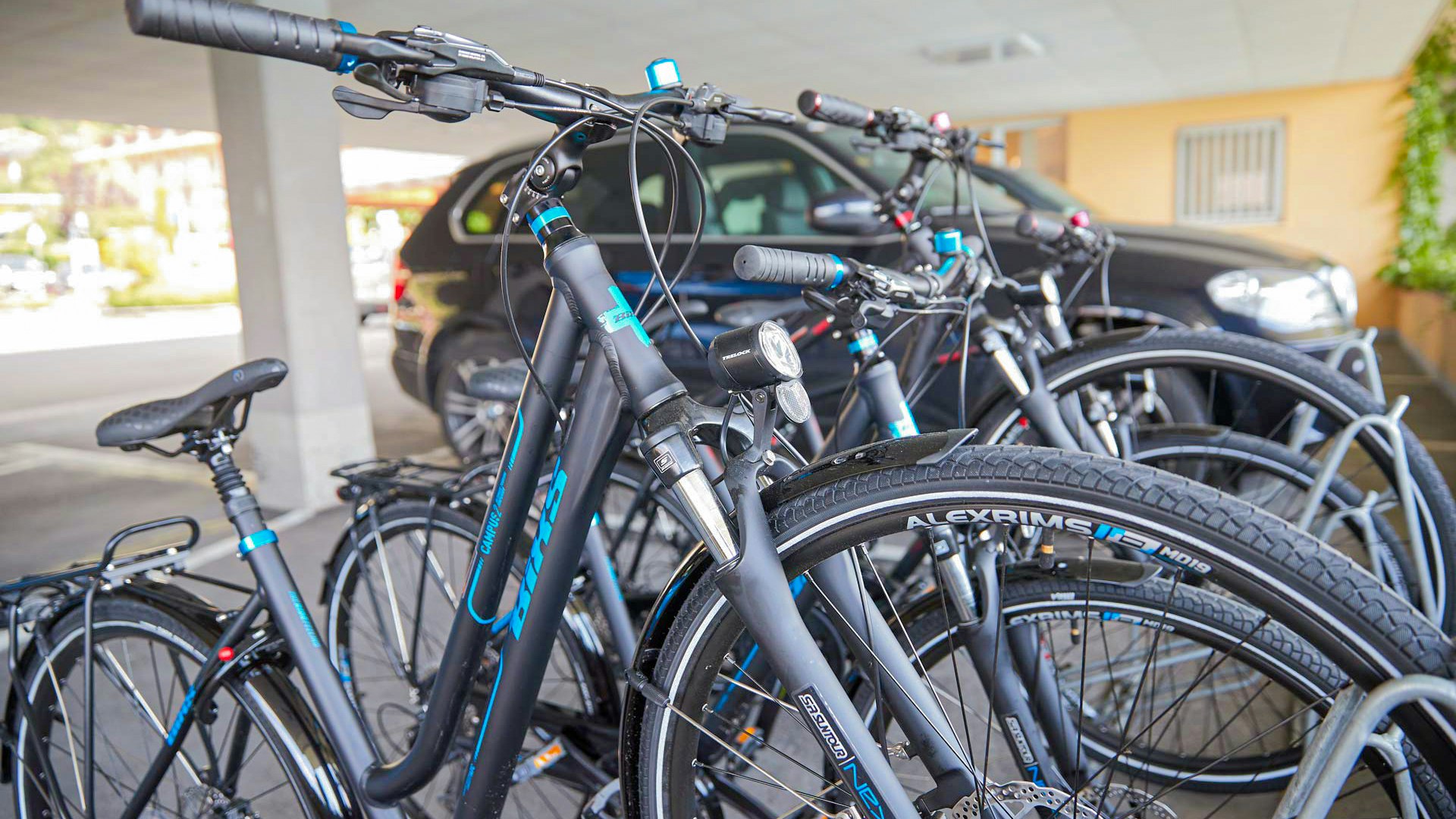 Mietvelos des Hotel BEATUS Vier Fahrräder in Fahrradständern, dahinter ein geparkte Auto