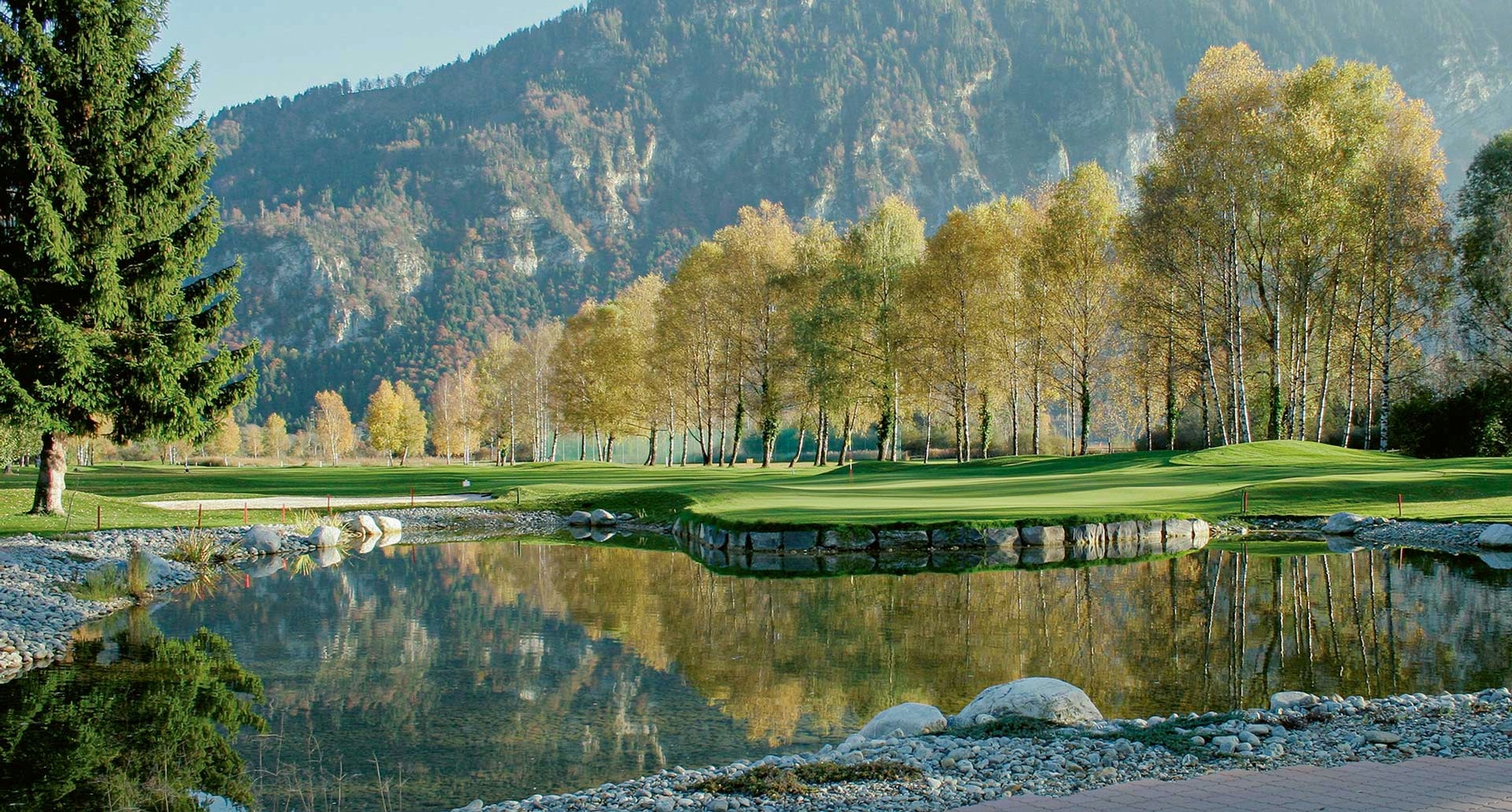 Ein Golfplatz mit einem künstlichem Teich und kurz getrimmtem Rasen mit Bäumen runderherum